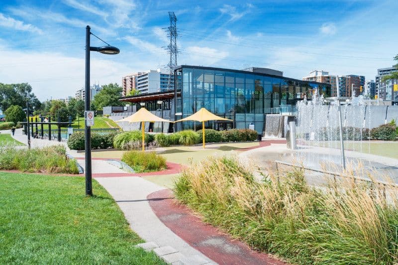 A park with a fountain and umbrellas in front of a building.
