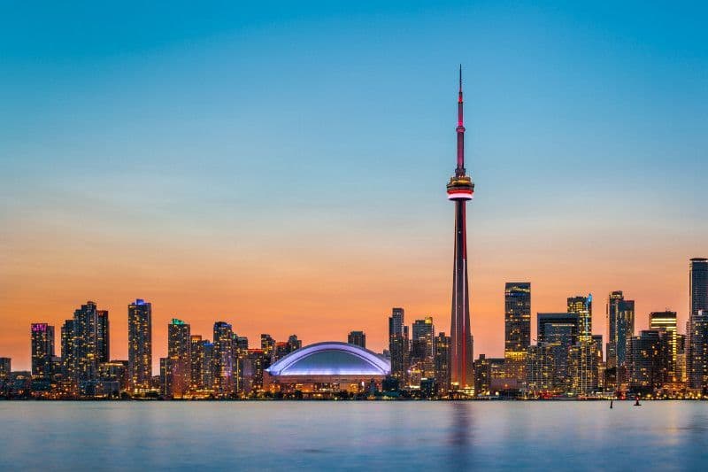 A city skyline with the cn tower in the foreground and a large body of water in the background.