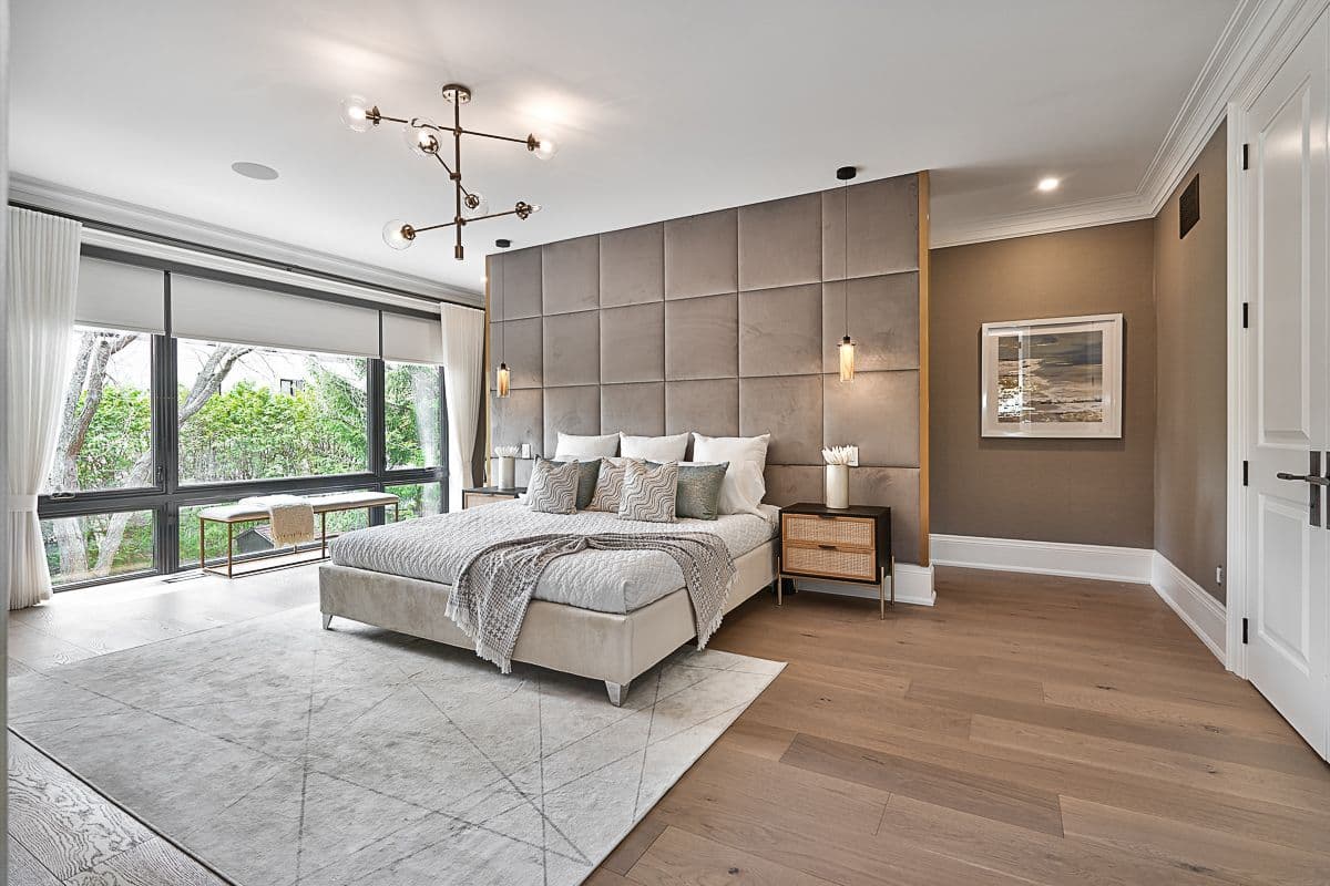 Large primary bedroom with neutral bedding, 2 side tables, a bench and a rug.